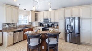 A modern kitchen with white cabinets, stainless steel appliances, a granite countertop, and pendant lighting. - Sun Realty ocean and sunrise views from Making Waves in Kill Devil Hills, NC (Kill Devil Hills)
