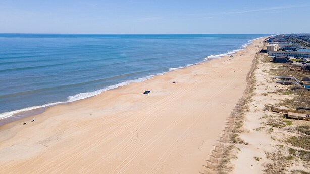 A beach with a long stretch of sand, a few people, and buildings along the shore. - Sun Realty ocean and sunrise views from Making Waves in Kill Devil Hills, NC (Kill Devil Hills)
