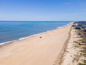Uma praia com uma extensa faixa de areia, algumas pessoas e edifícios à beira-mar.