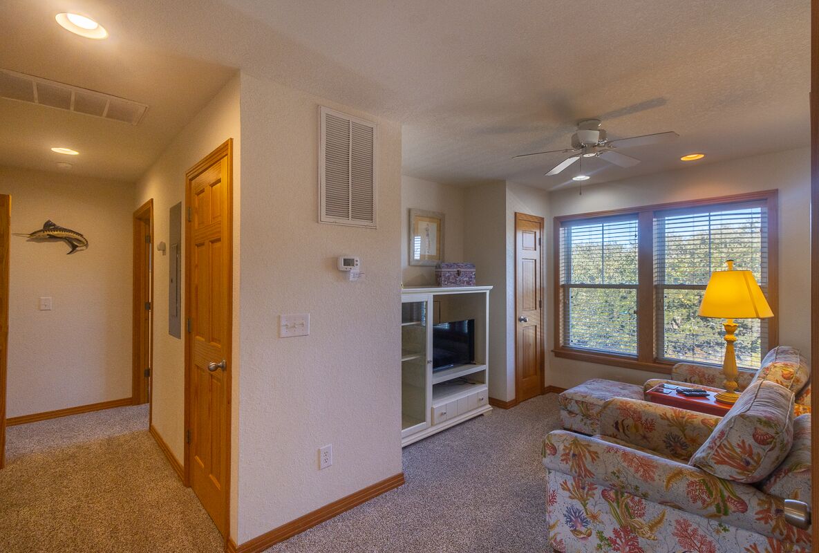 A living room with a ceiling fan, a TV on a stand, a sofa, and a window with blinds.