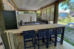 Eine Terrasse im Freien mit einem Holztisch, Stühlen, einem Whirlpool und einem Kühlschrank.