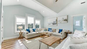 Un salon spacieux avec un grand canapé d’angle, une table basse en bois et une petite table d’appoint. De grandes fenêtres laissent entrer la lumière naturelle et offrent une vue sur l’extérieur.