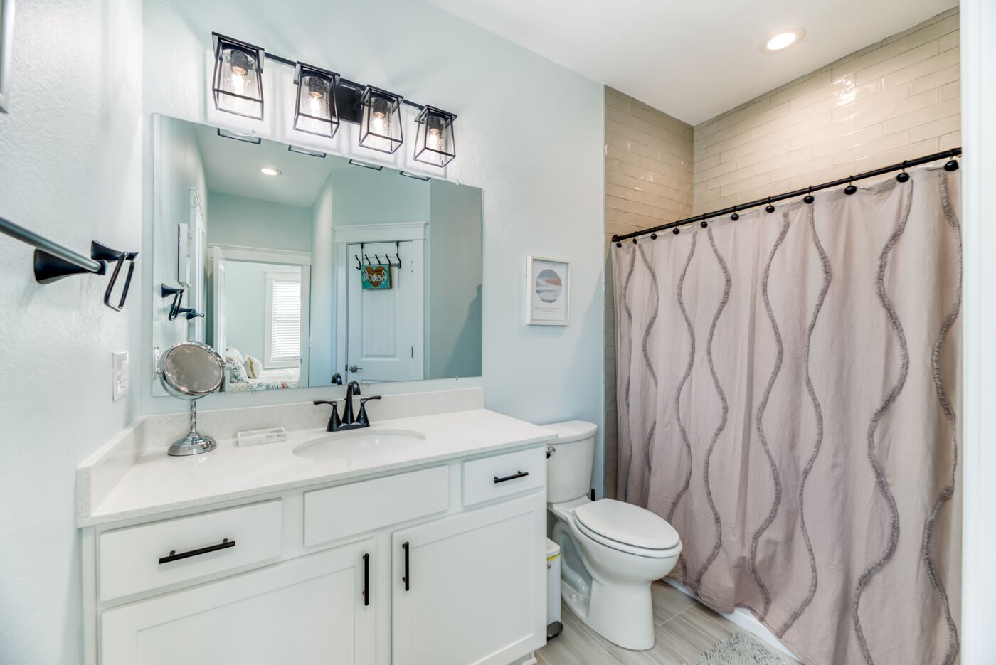 A bathroom with a white vanity, a mirror, a sink, a toilet, and a shower curtain.
