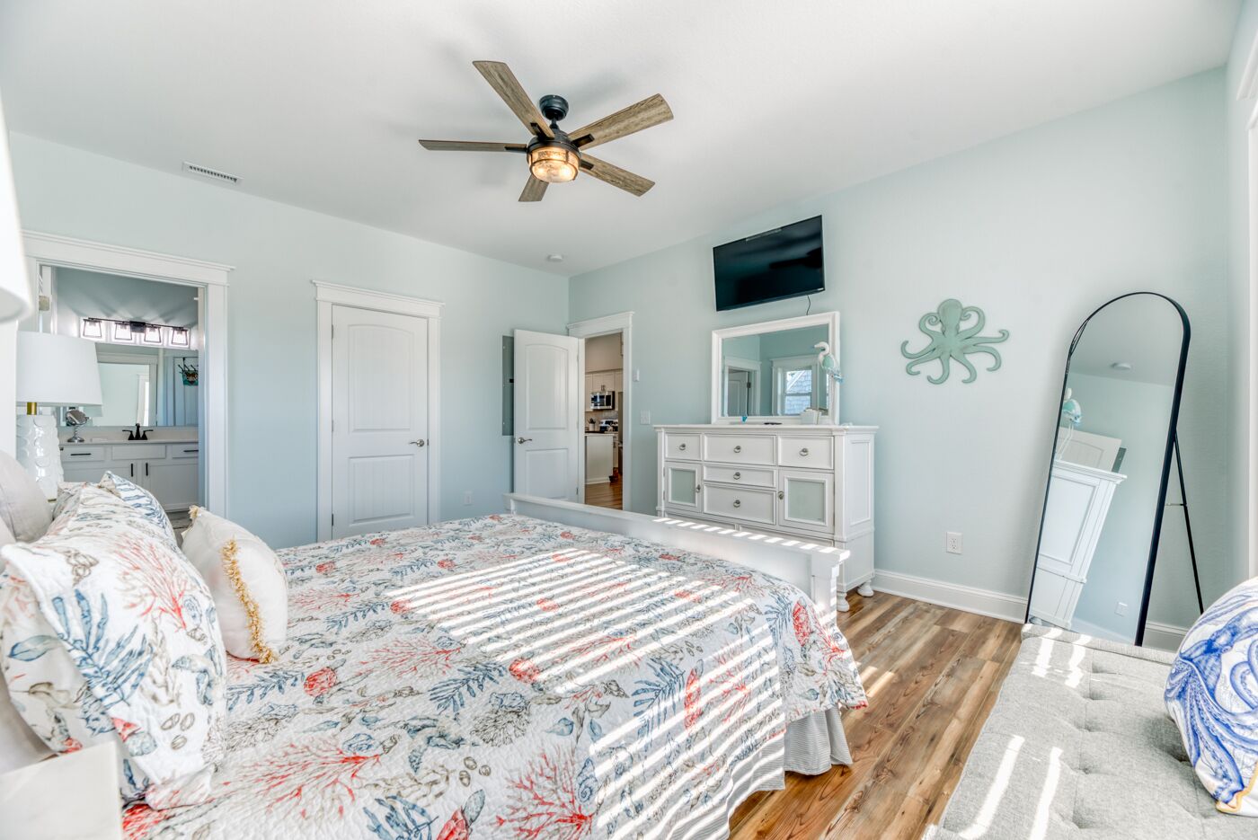 A bedroom with a bed, a ceiling fan, a dresser, a mirror, and a TV.