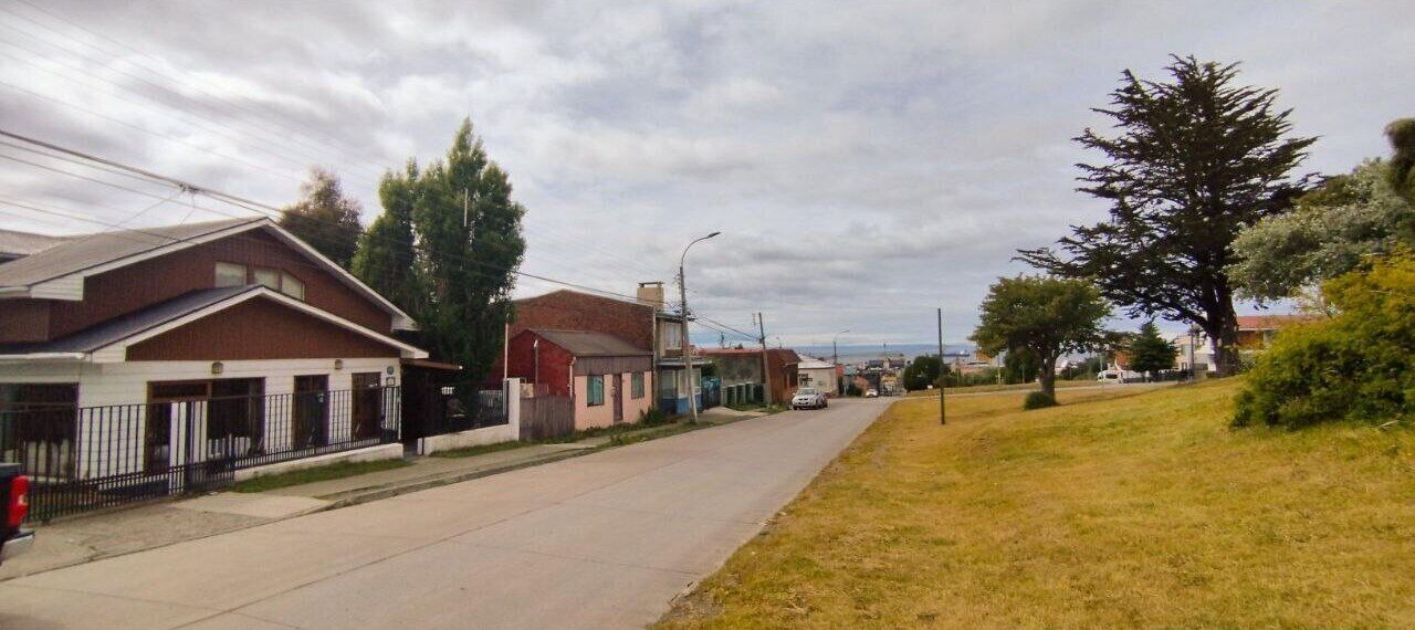 A residential street with houses, a sidewalk, and a grassy area.
