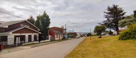 A residential street with houses, a sidewalk, and a grassy area.