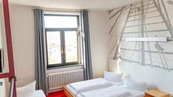 Habitación de hotel con dos camas, una ventana con cortinas, un radiador y una pared con un mural de temática náutica.