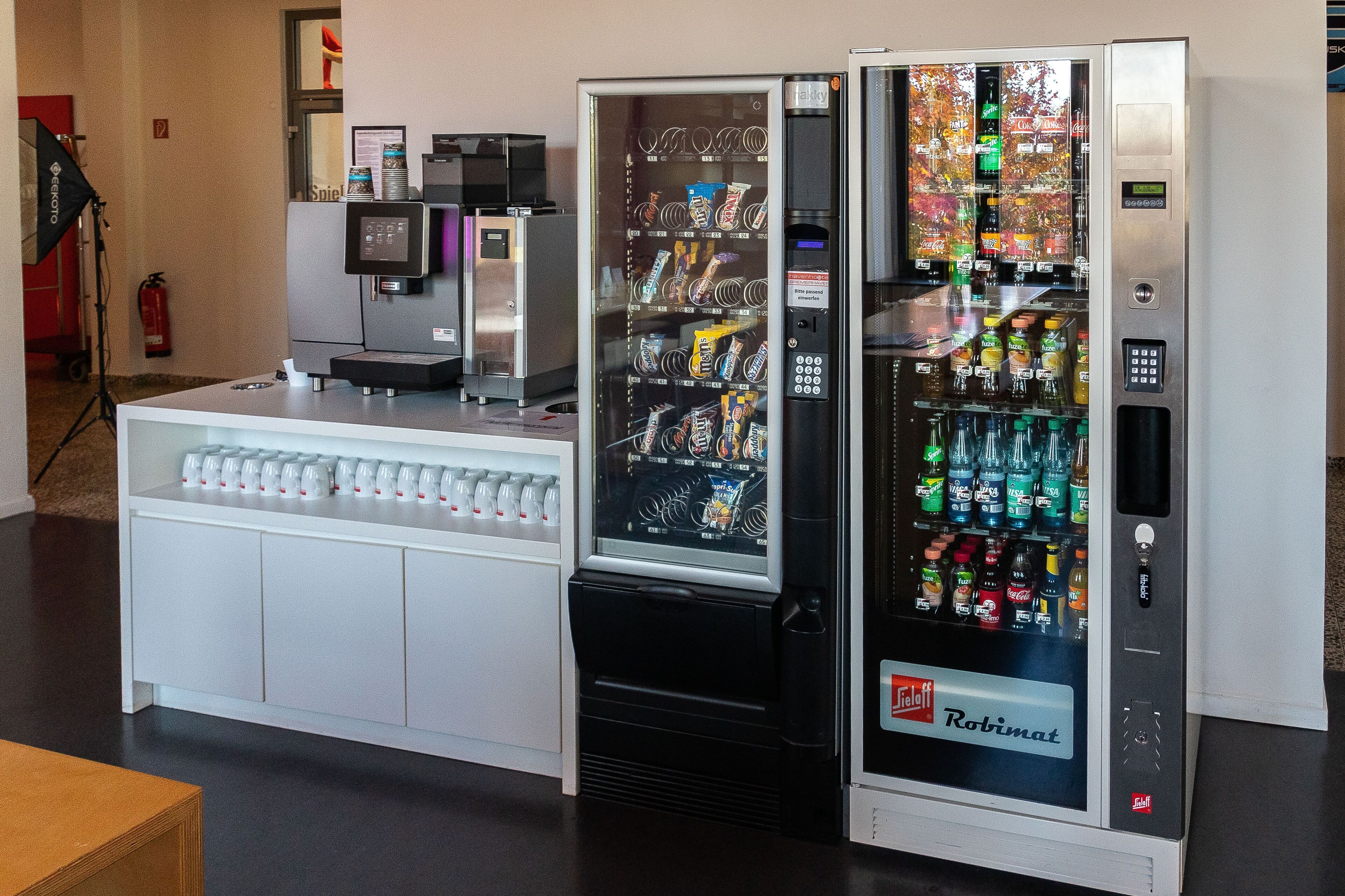 Zona con máquinas expendedoras que ofrecen una variedad de aperitivos y bebidas, incluyendo una máquina de la marca Robimatt.