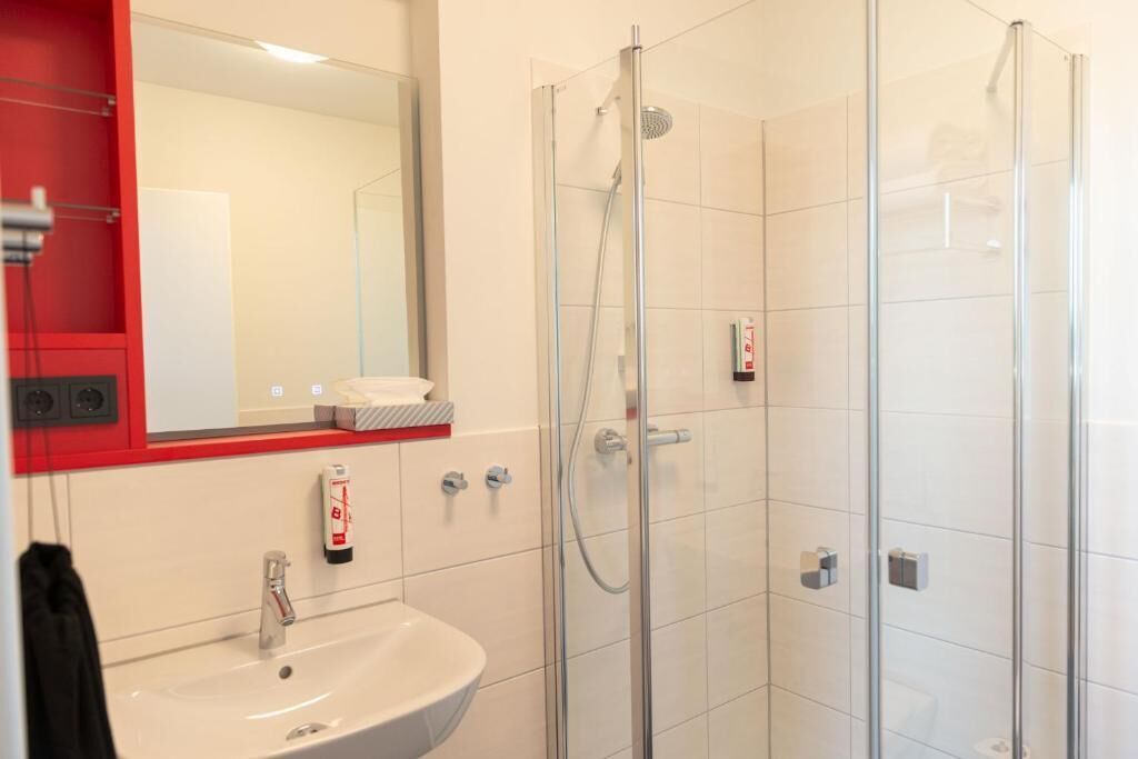 A modern bathroom with a glass-enclosed shower, a white sink, and a red-framed mirror.