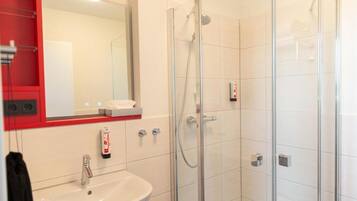 A modern bathroom with a glass-enclosed shower, a white sink, and a red-framed mirror.