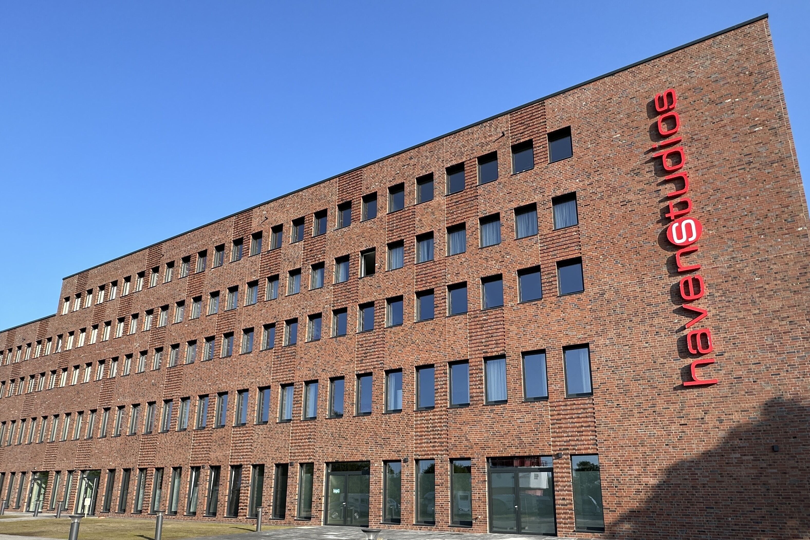 A modern brick building with multiple windows and a prominent red sign on the side.