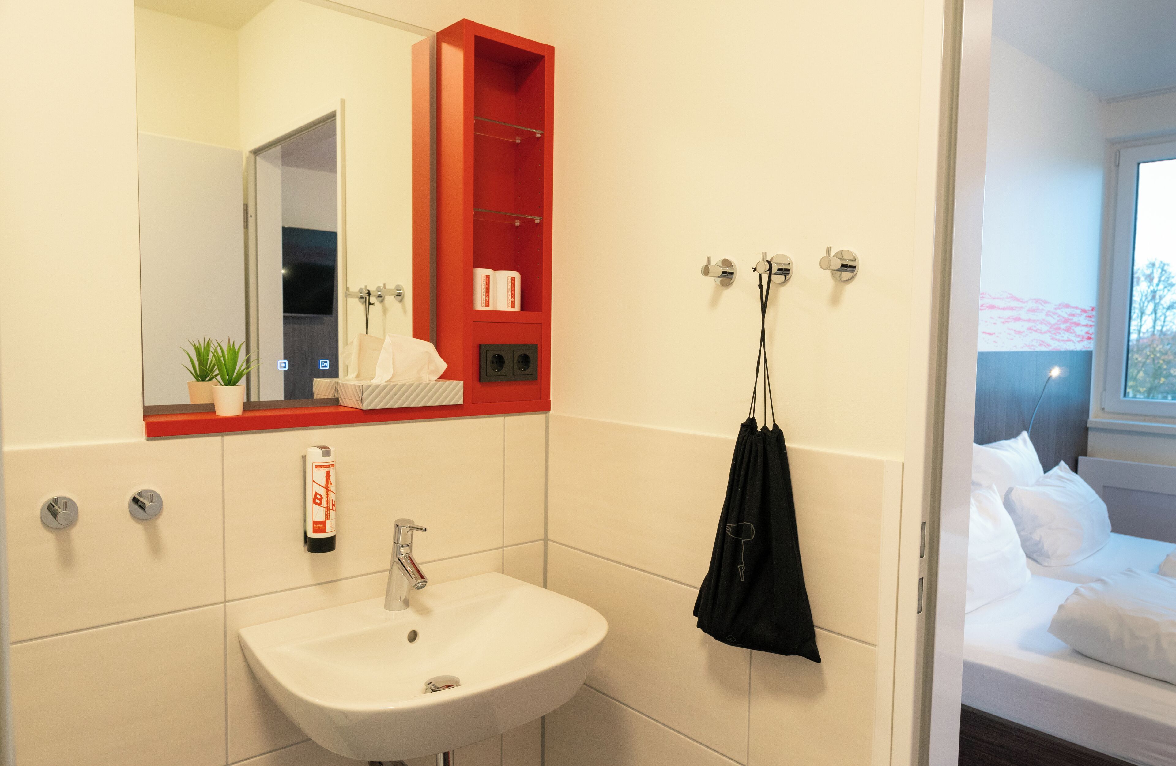 A modern bathroom with a white sink, a red medicine cabinet, and a black towel hanging on hooks.
