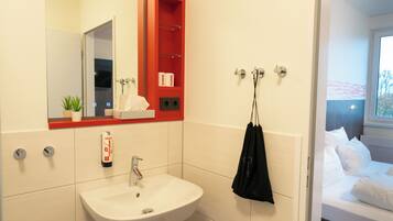A modern bathroom with a white sink, a red medicine cabinet, and a black towel hanging on hooks.
