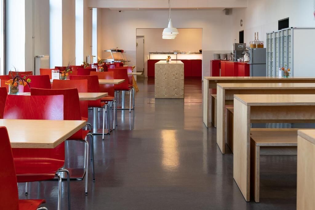 A modern dining area with red chairs and tables, a central island, and a kitchen in the background.