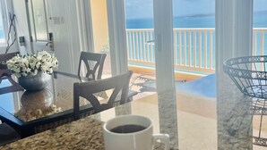 Ein Zimmer mit Glastisch, einer weißen Kaffeetasse, einer roten Rose und Blick auf den Ozean durch große Fenster.
