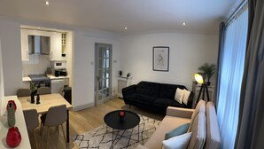 A modern living room with a black sofa, a dining table with chairs, and a kitchen area with a stove and microwave. - 2 single or 1 King bed in Notting Hill.. Super location for sightseeing London
 (London)
