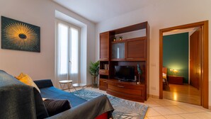 Una sala moderna con un sofá, televisor, mueble de madera y vista a una habitación verde a través de una puerta abierta.