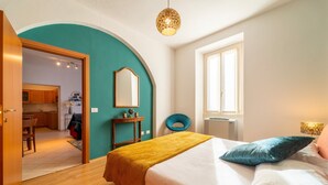 Un dormitorio con una cama, un espejo, una ventana y una puerta que da a una cocina.