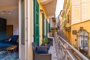 A narrow outdoor corridor with a blue sofa and wicker chairs, a small table with a plant, and a staircase leading to a yellow building. - Stairway Apartment by Wonderful Italy (Bellagio)