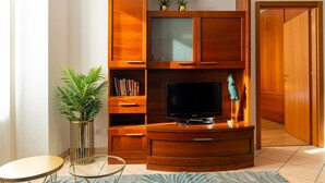 Una sala de estar con mueble de madera para entretenimiento, televisor de pantalla plana, mesa de centro de vidrio y una planta en maceta.