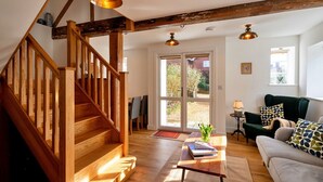 Un vaste espace de vie agrémenté d’un escalier en bois, d’un fauteuil vert et d’un canapé.