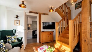 Un salon moderne avec un canapé vert, un escalier en bois et un téléviseur à écran plat.