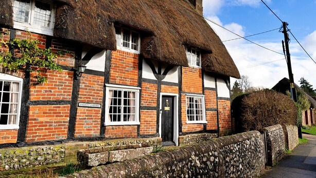 Une maison traditionnelle à colombages, avec un toit de chaume, un mur en pierre et une étroite entrée.