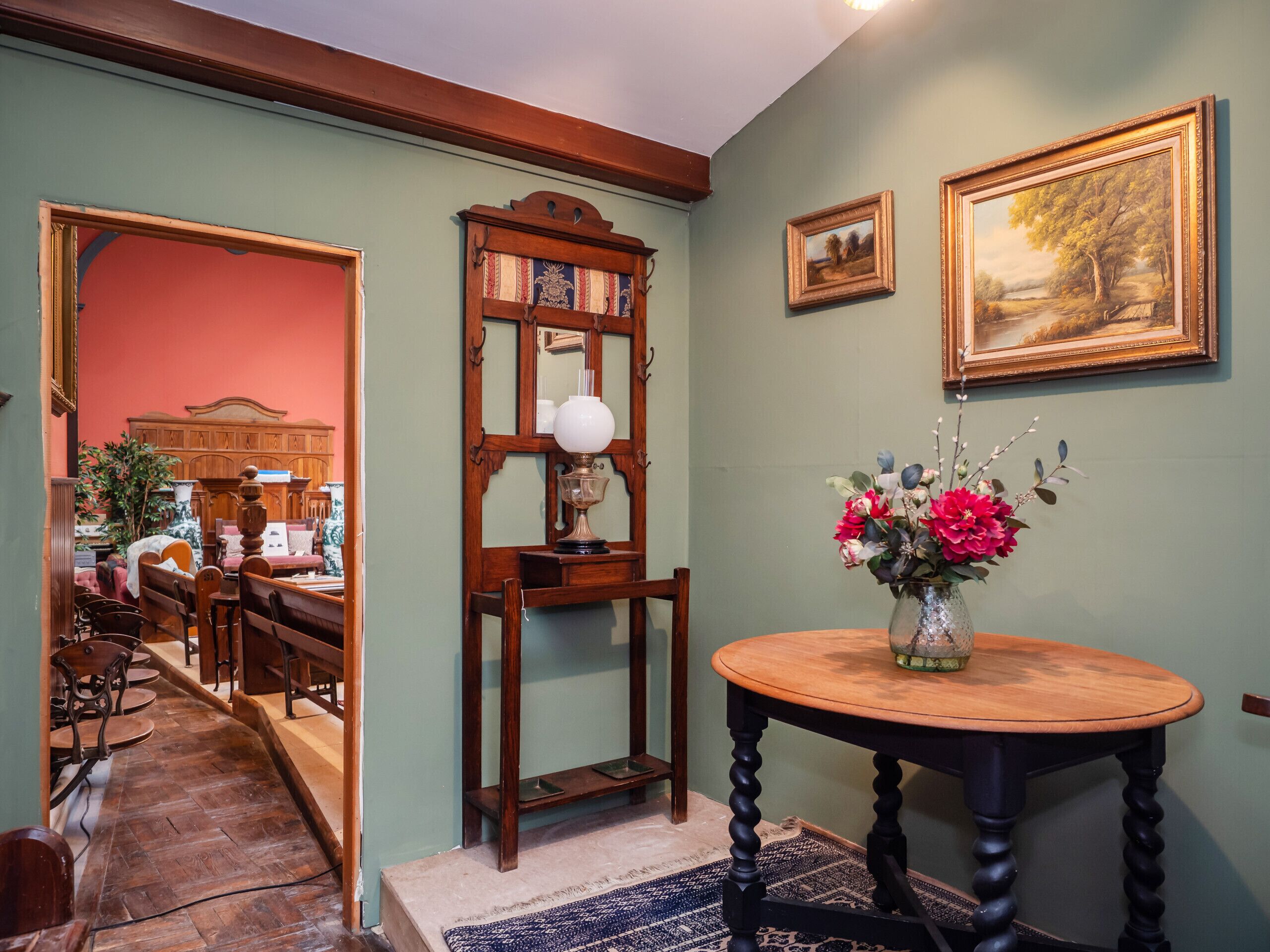 A room with a wooden table, a vase with flowers, and a framed painting on the wall.