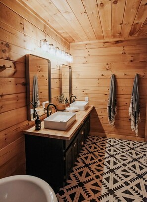 Ein Badezimmer in einer Holzhütte mit zwei Waschbecken, einem großen Spiegel und einem Musterboden.
