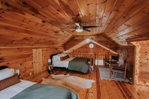 Ein gemütliches Schlafzimmer einer Holzhütte mit zwei Betten, einem Deckenventilator und einer kleinen Schreibtischzeile.