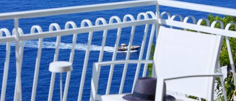 A balcony with a white railing, a table, and a chair. A boat is visible on the water in the background.
