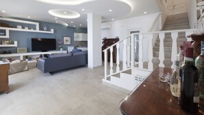 A modern living room with a flat-screen TV, sofa, and a dining area with a bar.