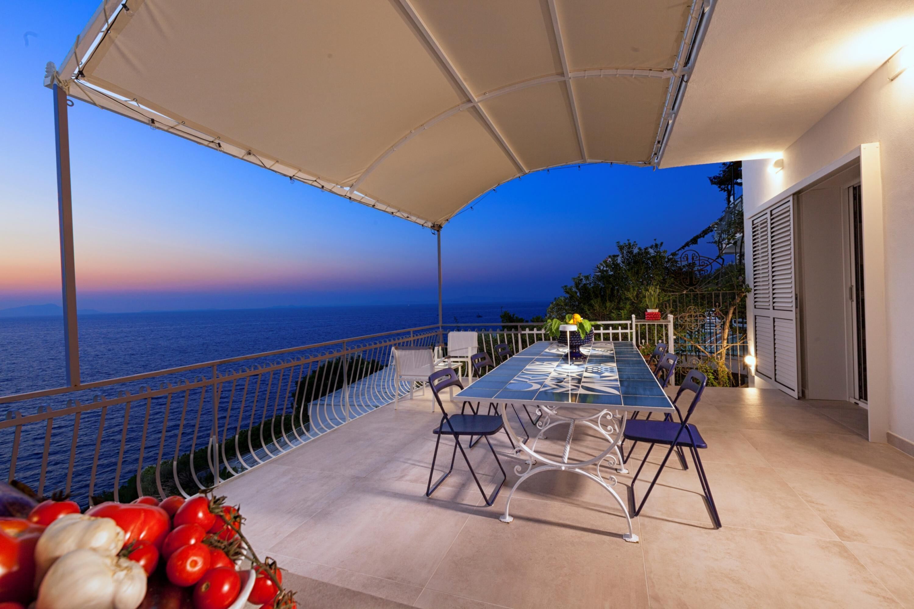 An outdoor dining area with a view of the sea, a covered table, and chairs.