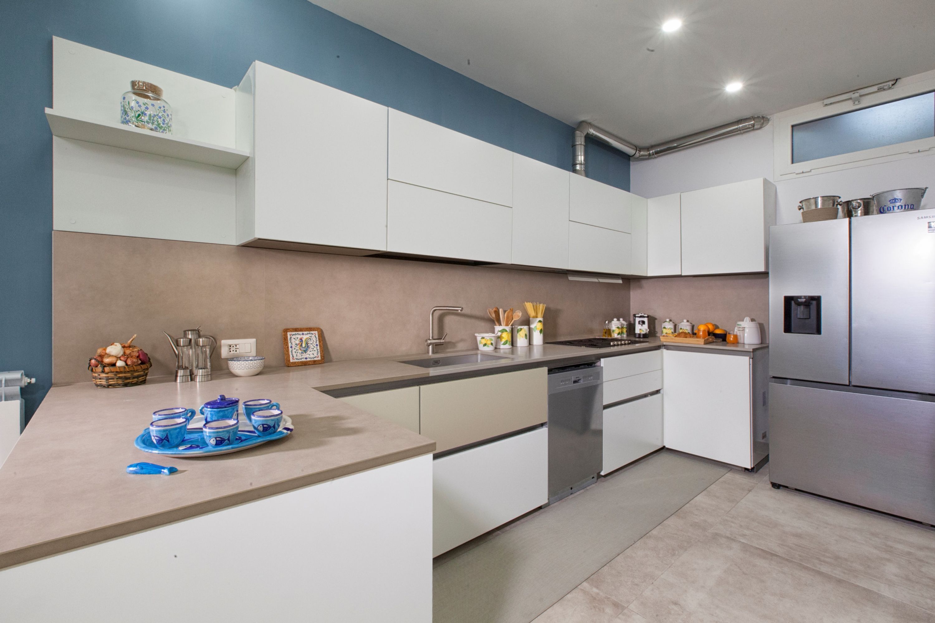 A modern kitchen with white cabinets, a stainless steel refrigerator, and a countertop with kitchenware.