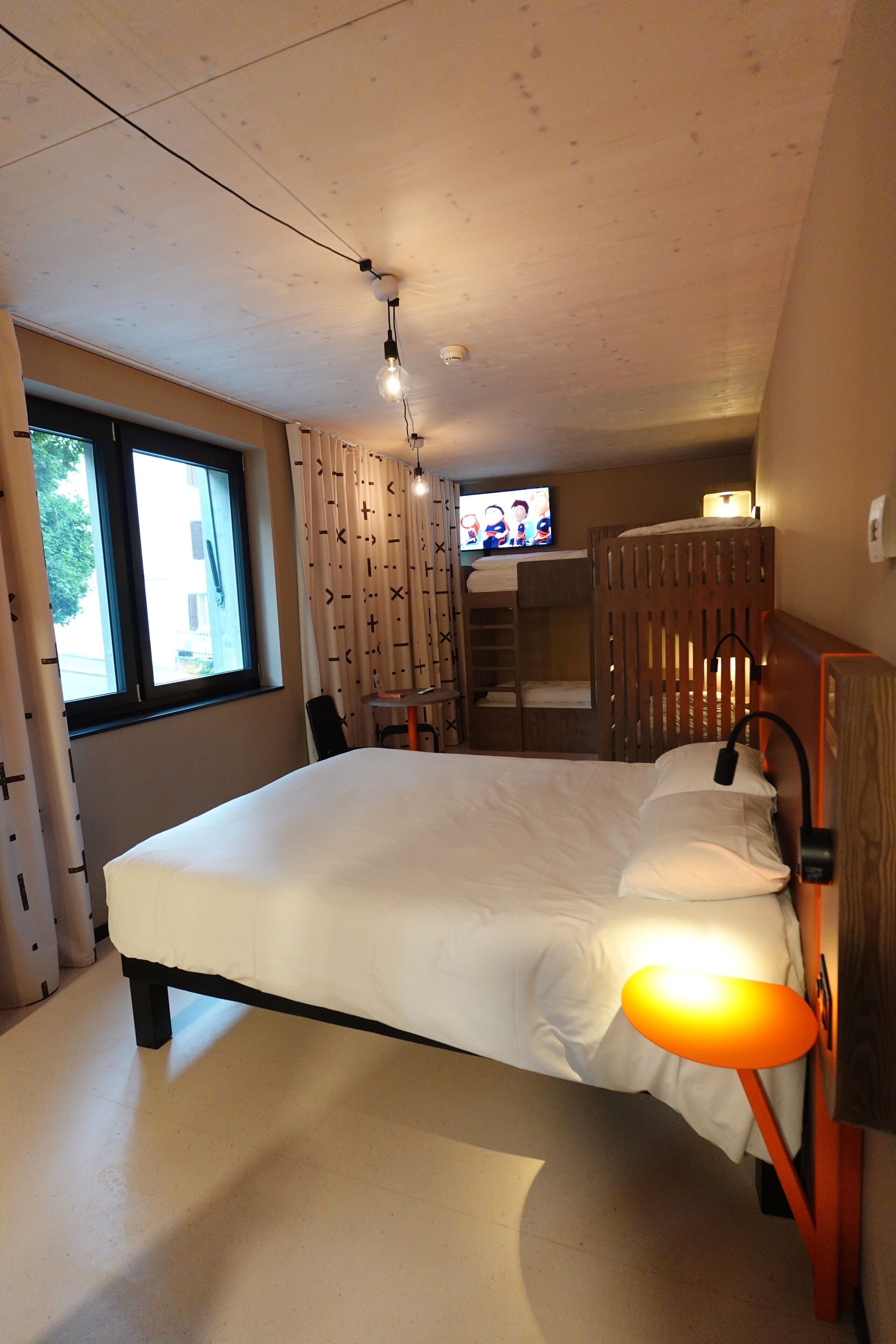 A bedroom with a bed, a TV, a desk, and a window.