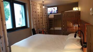 A bedroom with a bed, a TV, a desk, and a window.