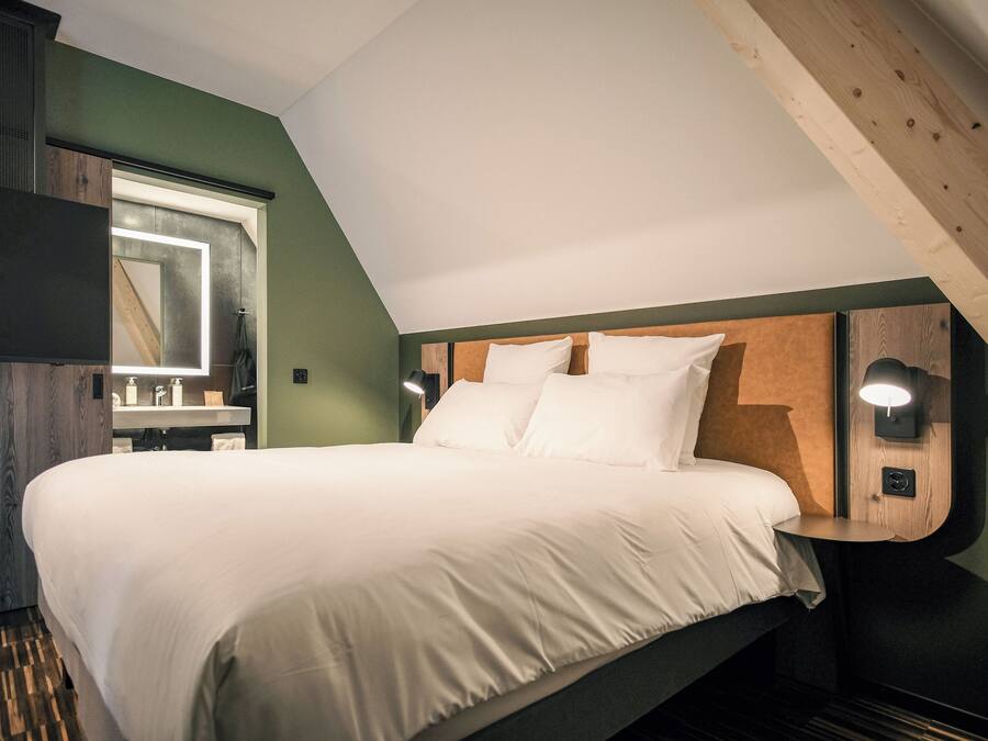 A bedroom with a large bed, a built-in headboard, a bedside table with a lamp, and a mirror above the sink.