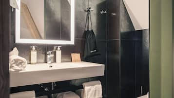 Ein modernes Badezimmer mit einem großen Spiegel, einem Waschbecken und einer Toilette. Auf dem Waschbeckenbrett liegen Handtücher und Pflegeprodukte.