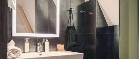 A modern bathroom with a large mirror, a sink, and a toilet. There are towels and toiletries on the sink counter.