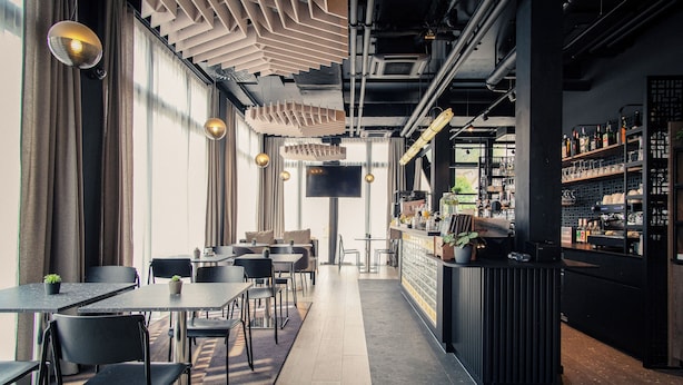 A modern restaurant with a bar area, wooden flooring, and black chairs. - Hota Hotel Saint-Imier (Saint-Imier)