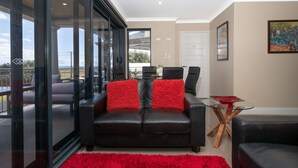 A modern living room with a black leather sofa, red cushions, a glass coffee table, and a red rug. - Ocean View Executive Apartment 4 (Geographe)