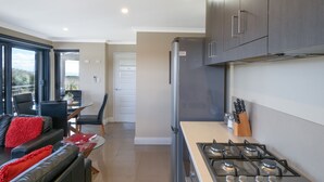 A modern kitchen with a gas stove, a refrigerator, and a dining area with a glass table and chairs. - Ocean View Executive Apartment 4 (Geographe)