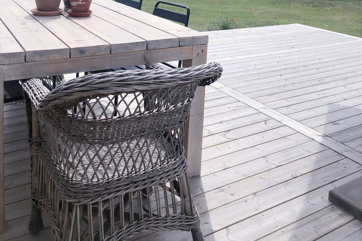 A wooden deck with a table and chairs, overlooking a body of water with a bridge in the distance.