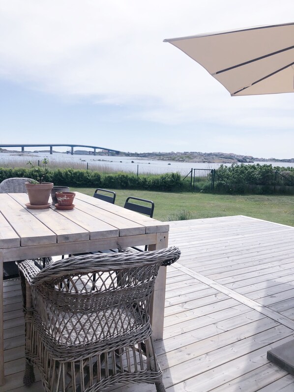 A wooden deck with a table and chairs, overlooking a body of water with a bridge in the distance. - Hönö Sjöbodar (Hono)