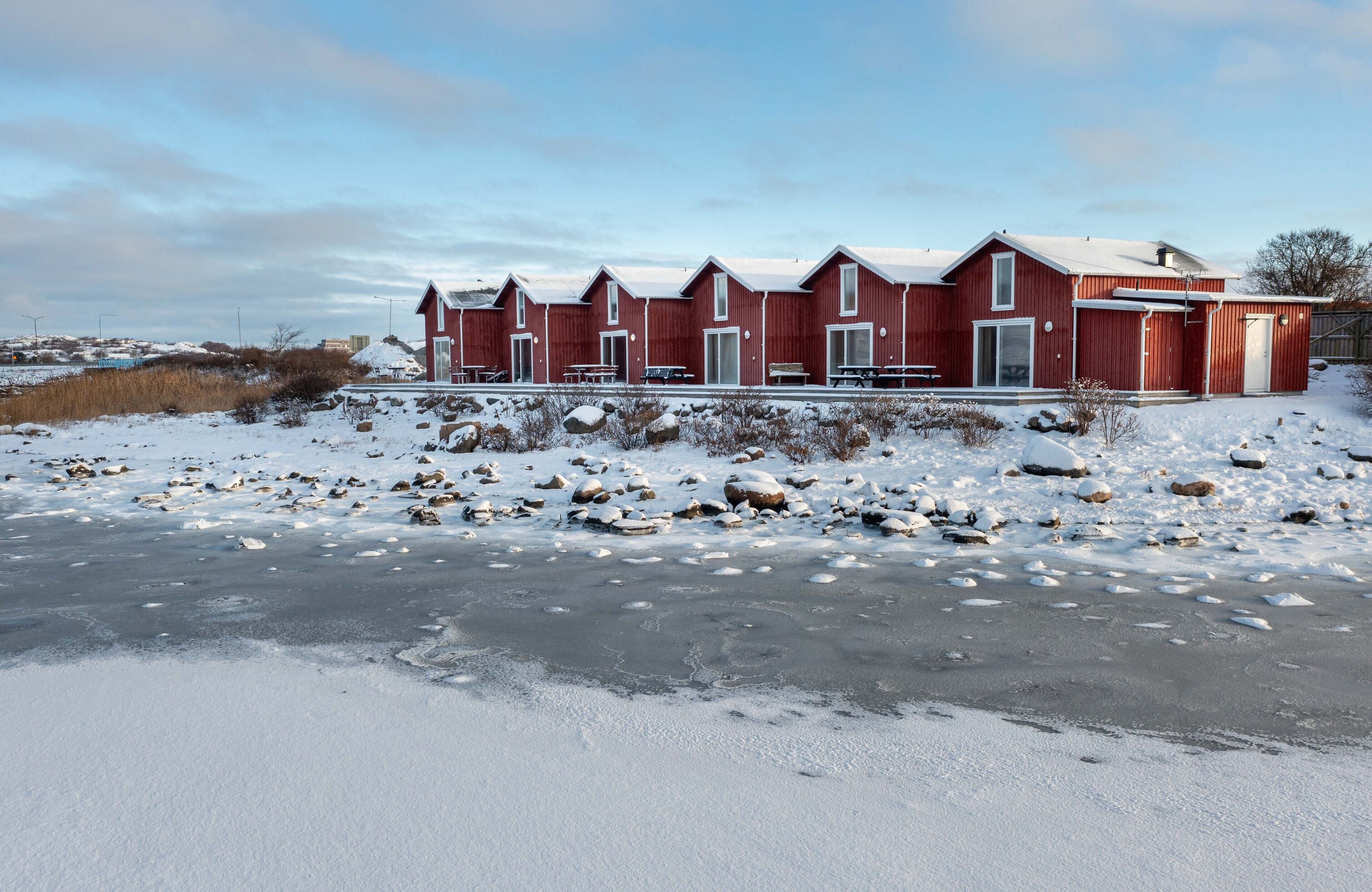 A row of red cabins with a snow-covered landscape and a frozen body of water in the foreground.