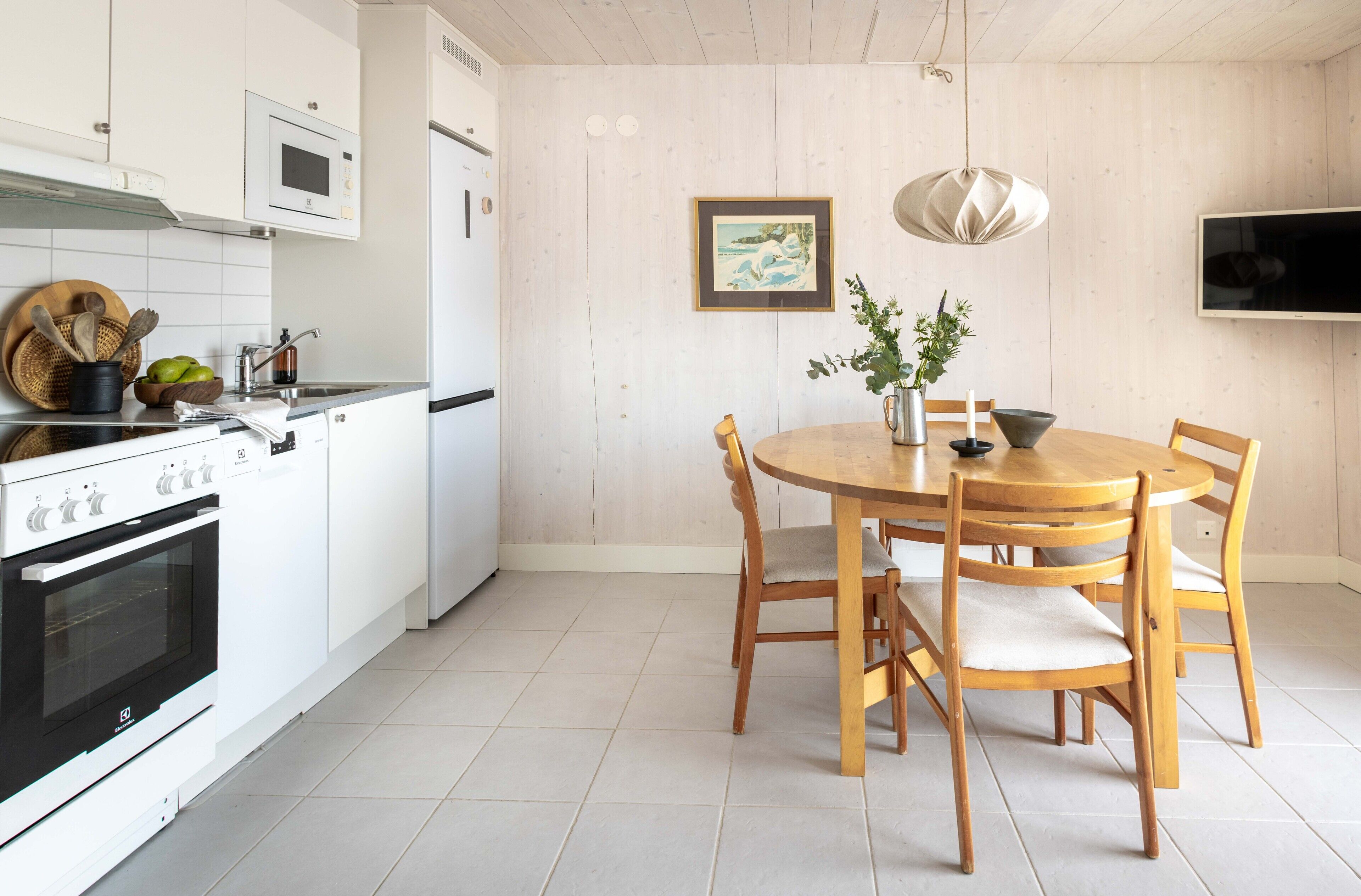 A modern kitchen with white cabinetry, a wooden dining table with four chairs, and a hanging pendant light.