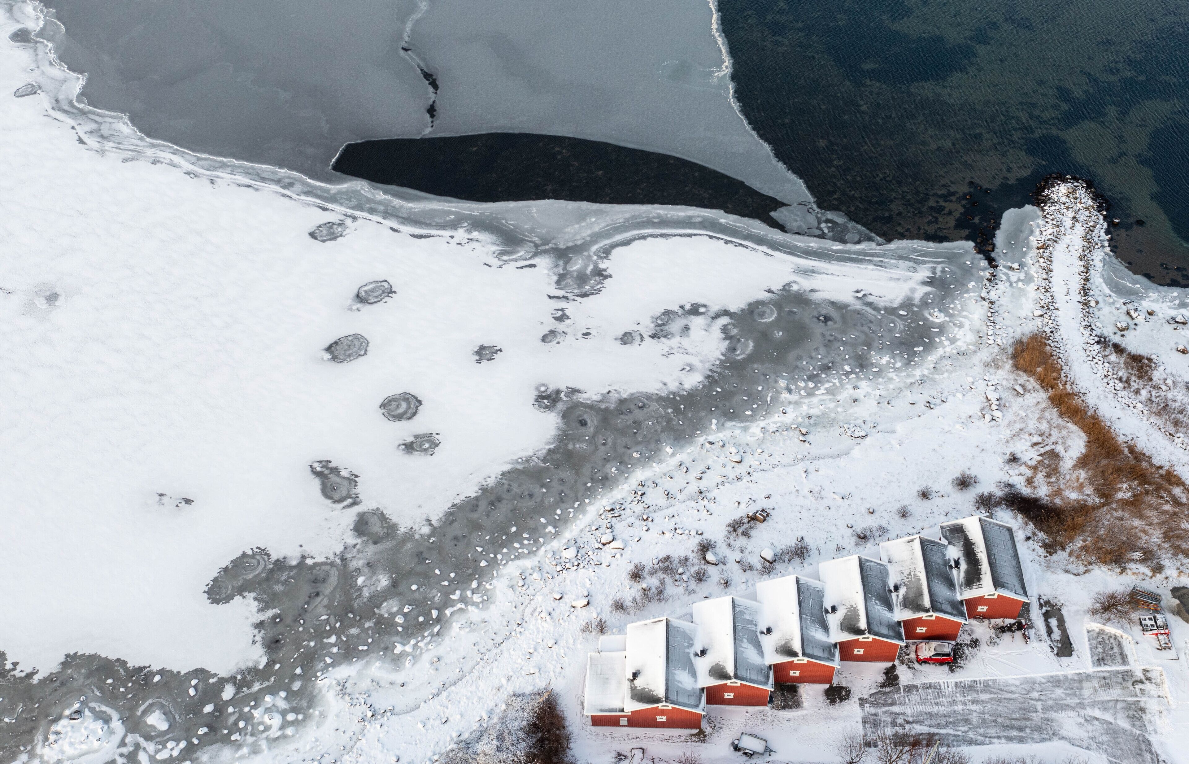 An aerial view of a snow-covered landscape with a series of red-roofed buildings aligned in a row.