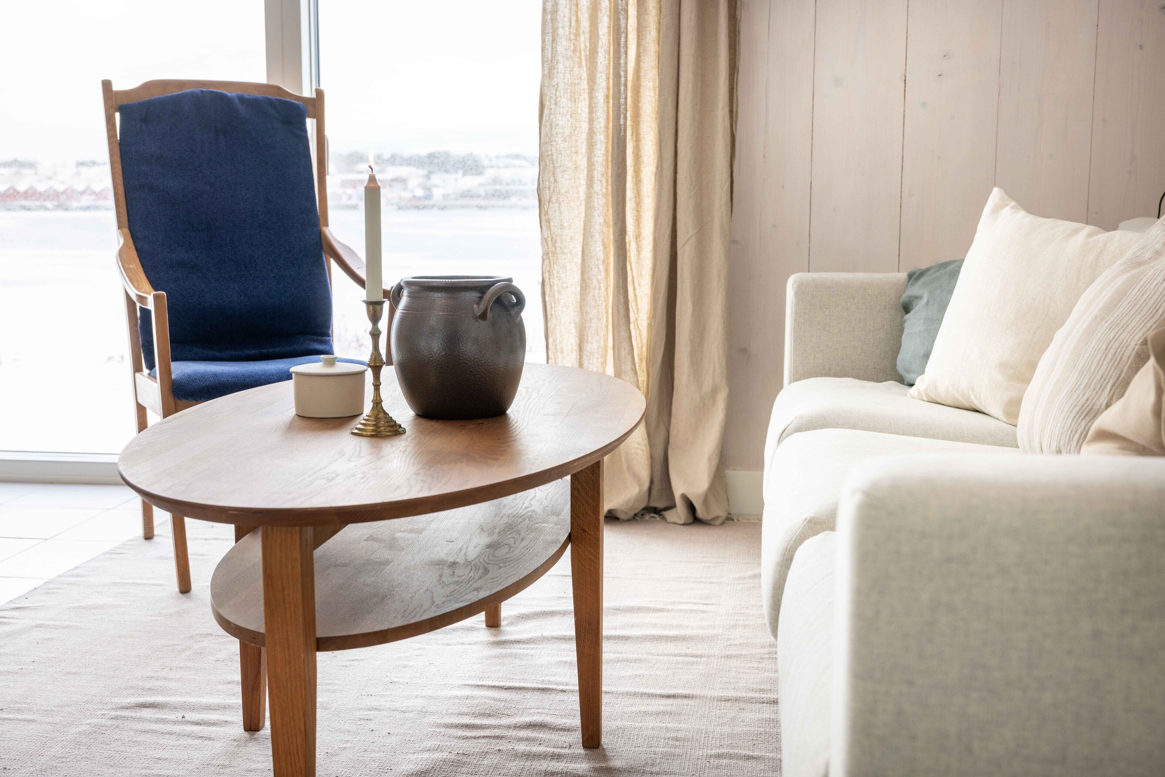 Ein Zimmer mit einem runden Holztisch, einem blauen Stuhl, einem weißen Sofa und Blick auf eine verschneite Landschaft durch ein Fenster.