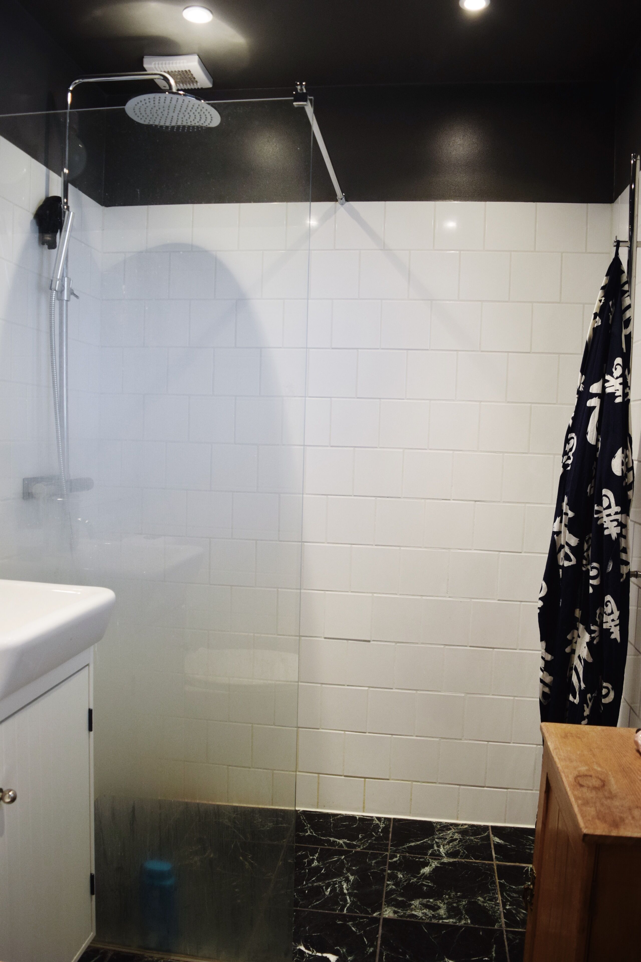 A bathroom with a shower, white tiled walls, a marble floor, and a wooden stool.