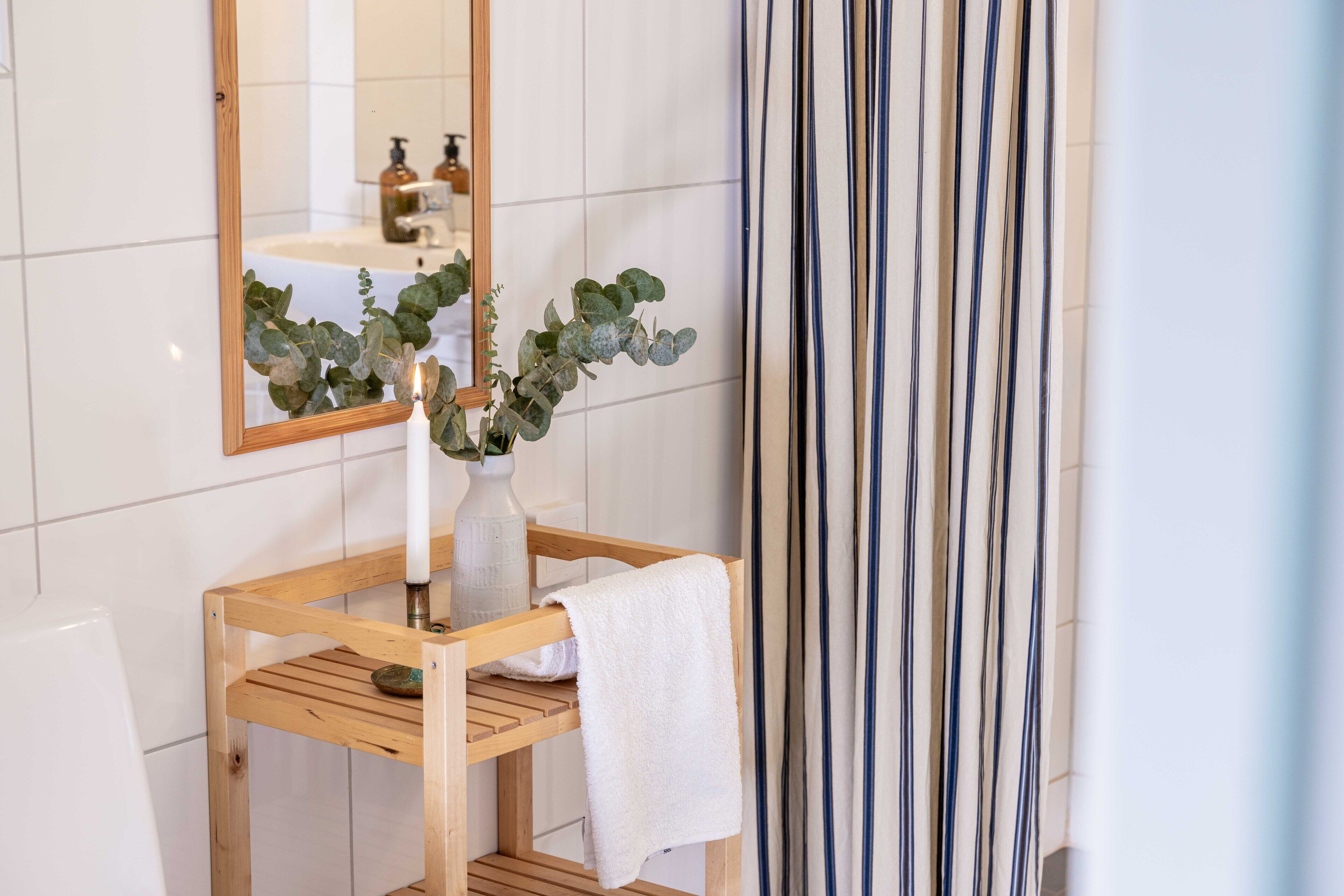 Un bagno con un mobile lavabo in legno, uno specchio, una pianta in vaso e una tenda a righe.